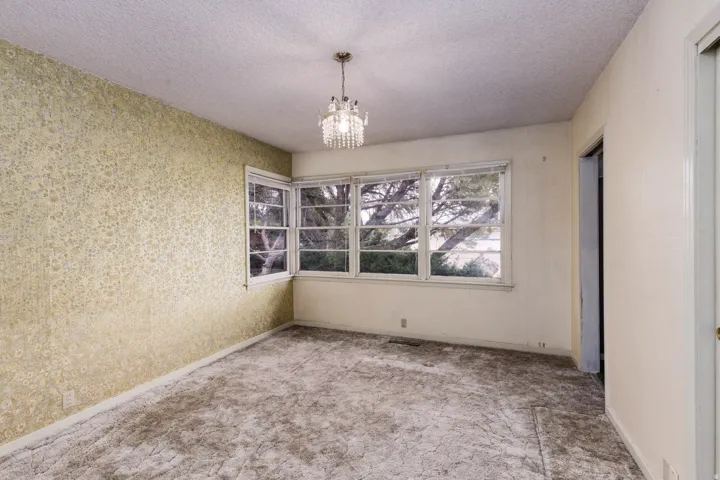 Unfurnished dining area featuring hanging lights, a textured ceiling, carpet, and wallpapered walls
