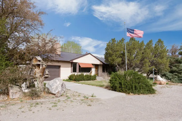 View of front of home featuring an attached garage, a metal roof, a chimney, and driveway