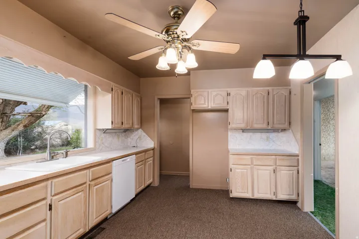 Kitchen featuring light countertops, a ceiling fan, white dishwasher, and light wood finish cabinets