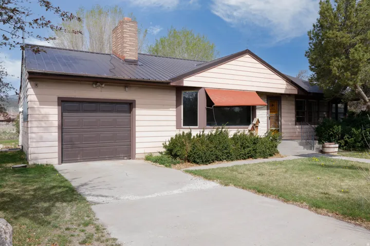 Ranch-style home featuring an attached garage, driveway, a front yard, a metal roof, and a chimney