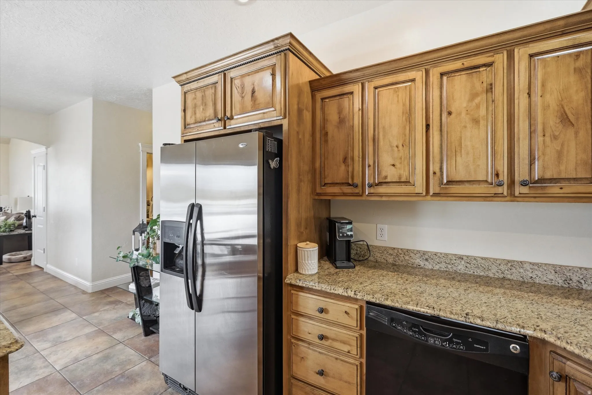 Kitchen featuring stainless steel refrigerator with ice dispenser, dishwasher, light stone countertops, and wood finish cabinetry