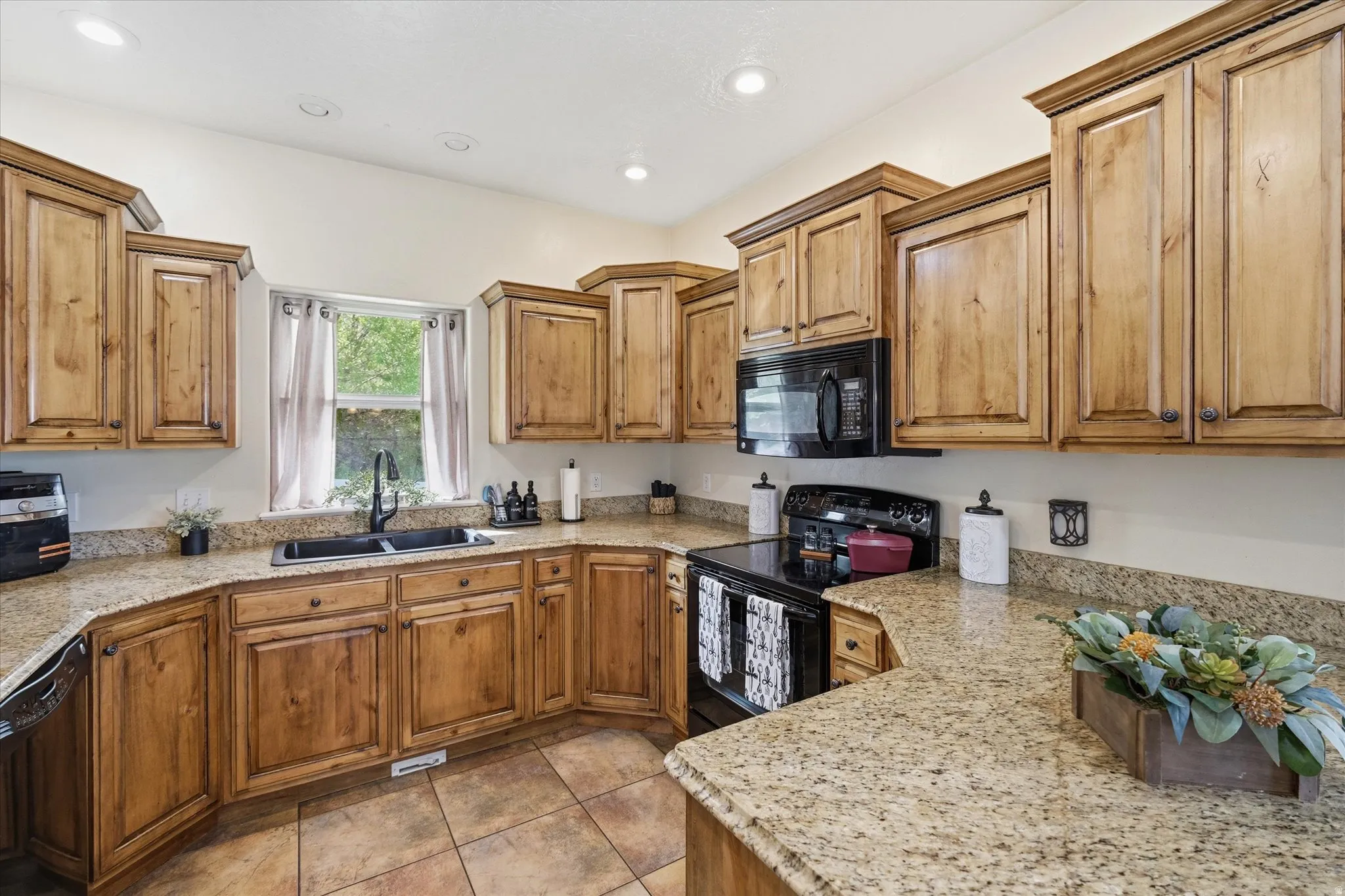 Kitchen with black appliances, wood finish cabinetry, light stone counters, light tile patterned floors, and recessed lighting