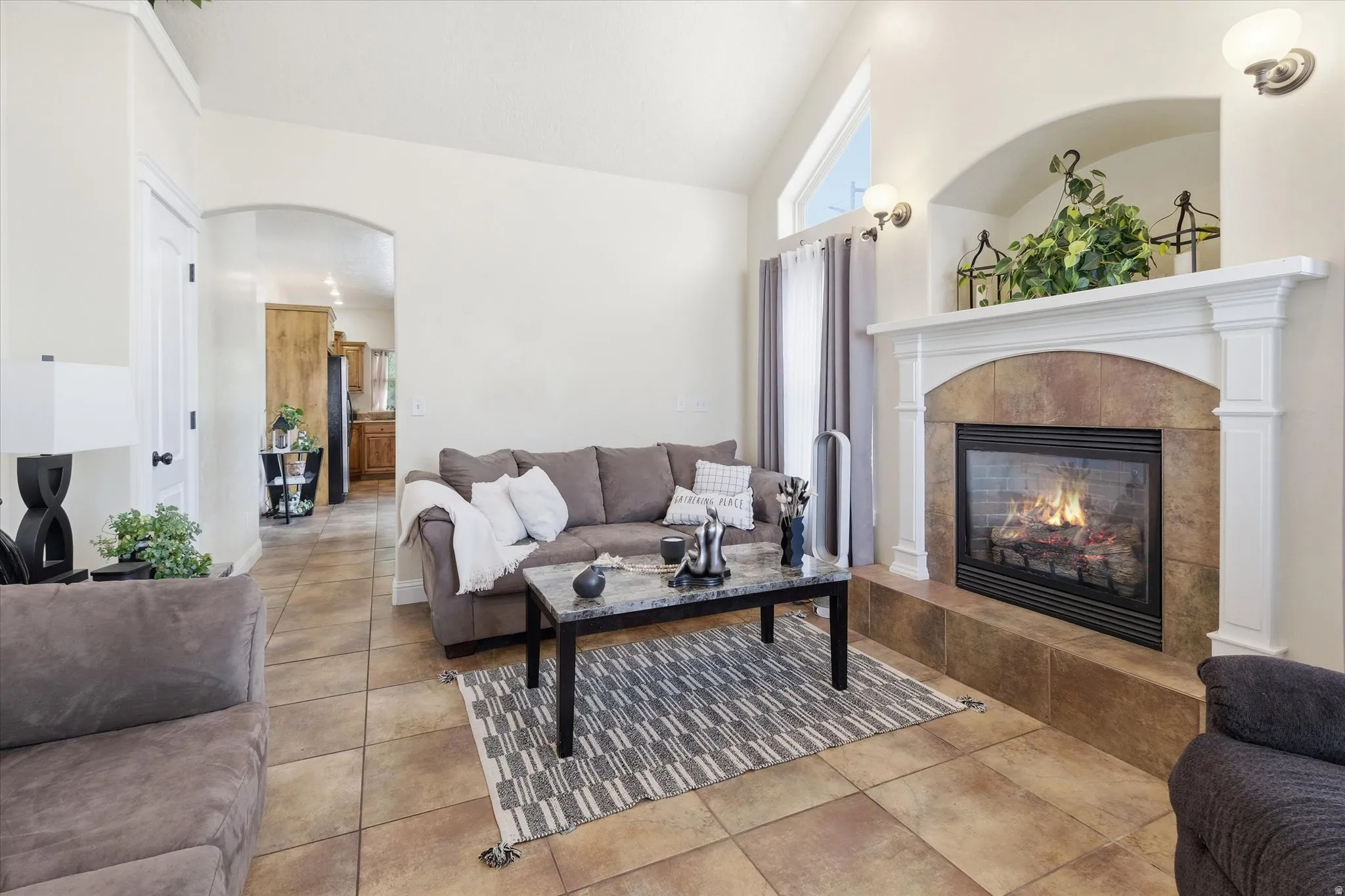 Living room featuring arched walkways, vaulted ceiling, a tiled fireplace, and light tile patterned floors