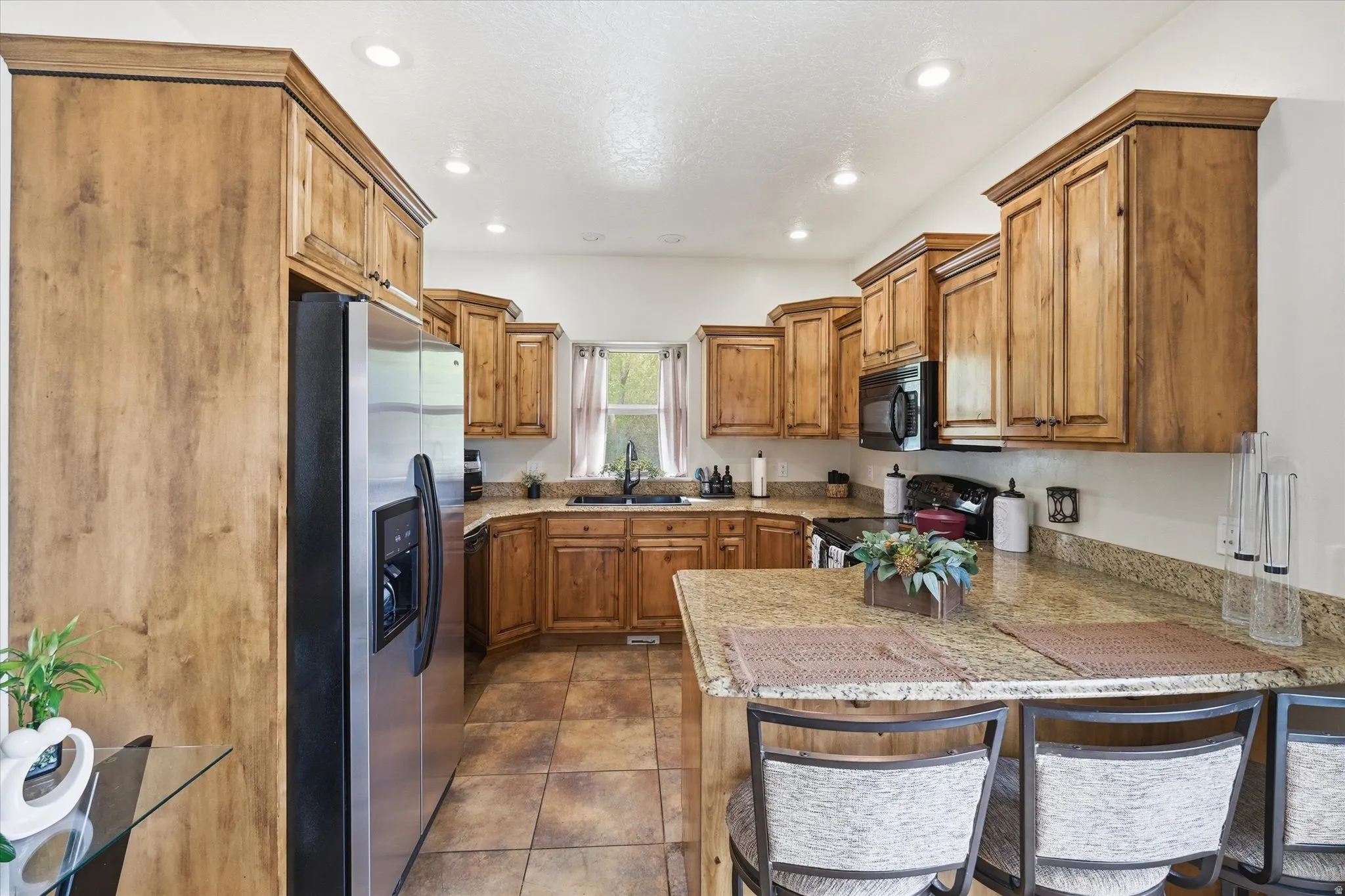 Kitchen with a kitchen bar, wood finish cabinetry, a peninsula, stainless steel refrigerator with ice dispenser, and electric stove