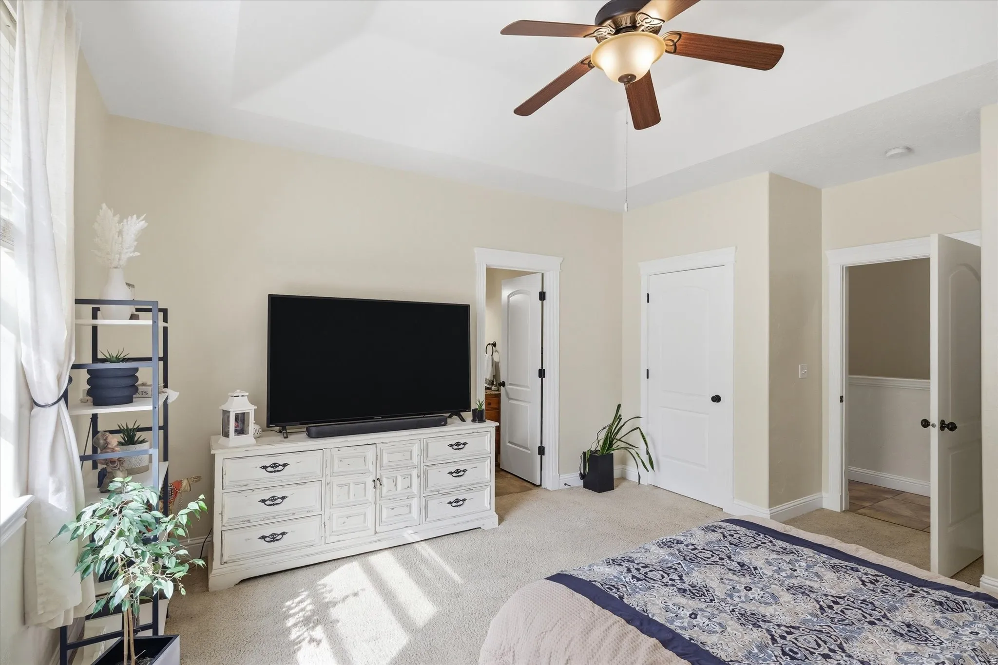 Bedroom featuring light colored carpet, ceiling fan, a tray ceiling, and ensuite bathroom