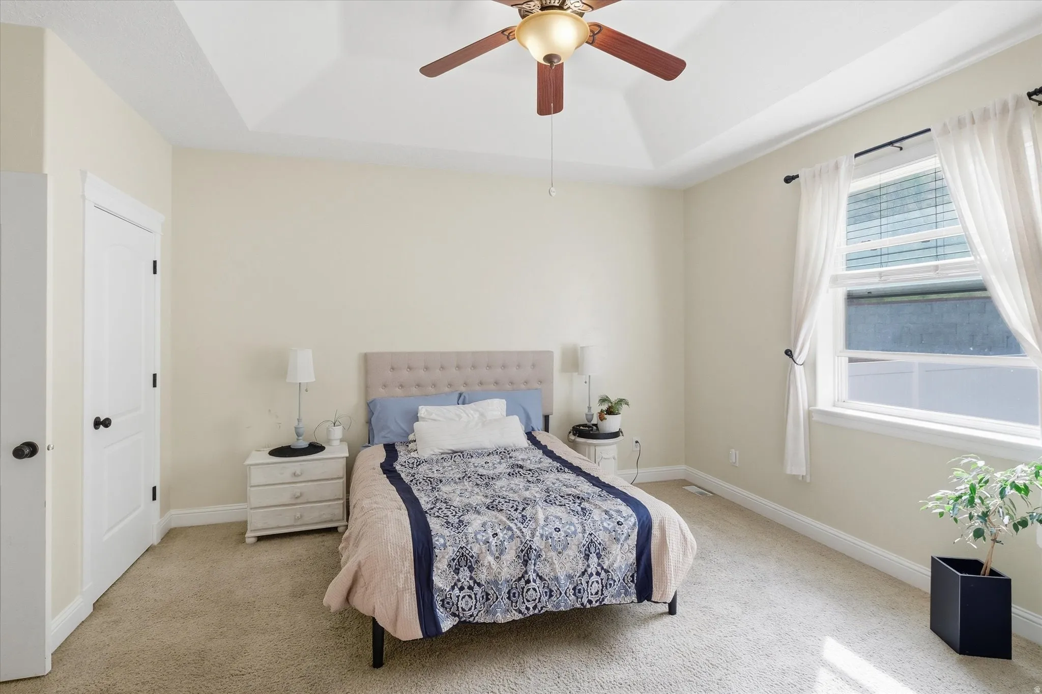 Bedroom with light carpet, a tray ceiling, and ceiling fan