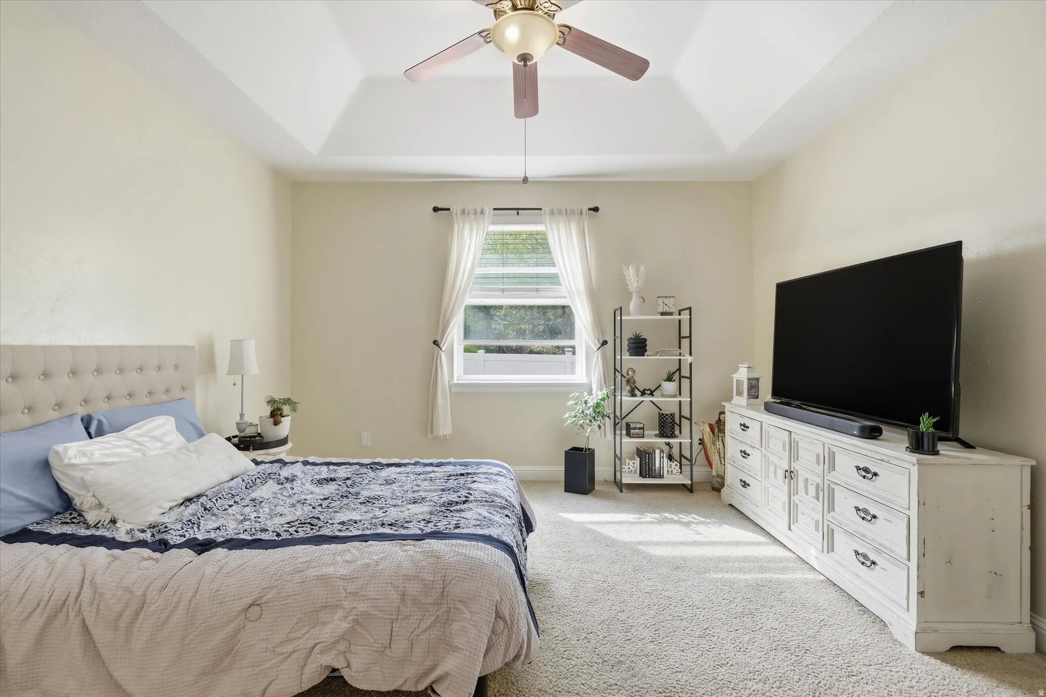 Bedroom featuring a tray ceiling, light colored carpet, and ceiling fan