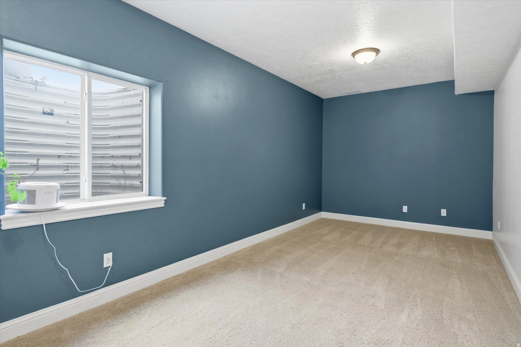 Empty room with light carpet and a textured ceiling