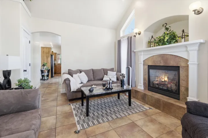 Living room featuring arched walkways, vaulted ceiling, a tiled fireplace, and light tile patterned floors