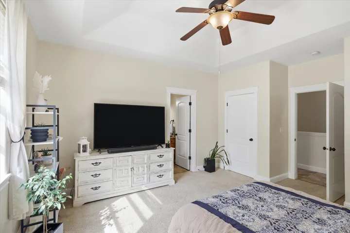 Bedroom featuring light colored carpet, ceiling fan, a tray ceiling, and ensuite bathroom