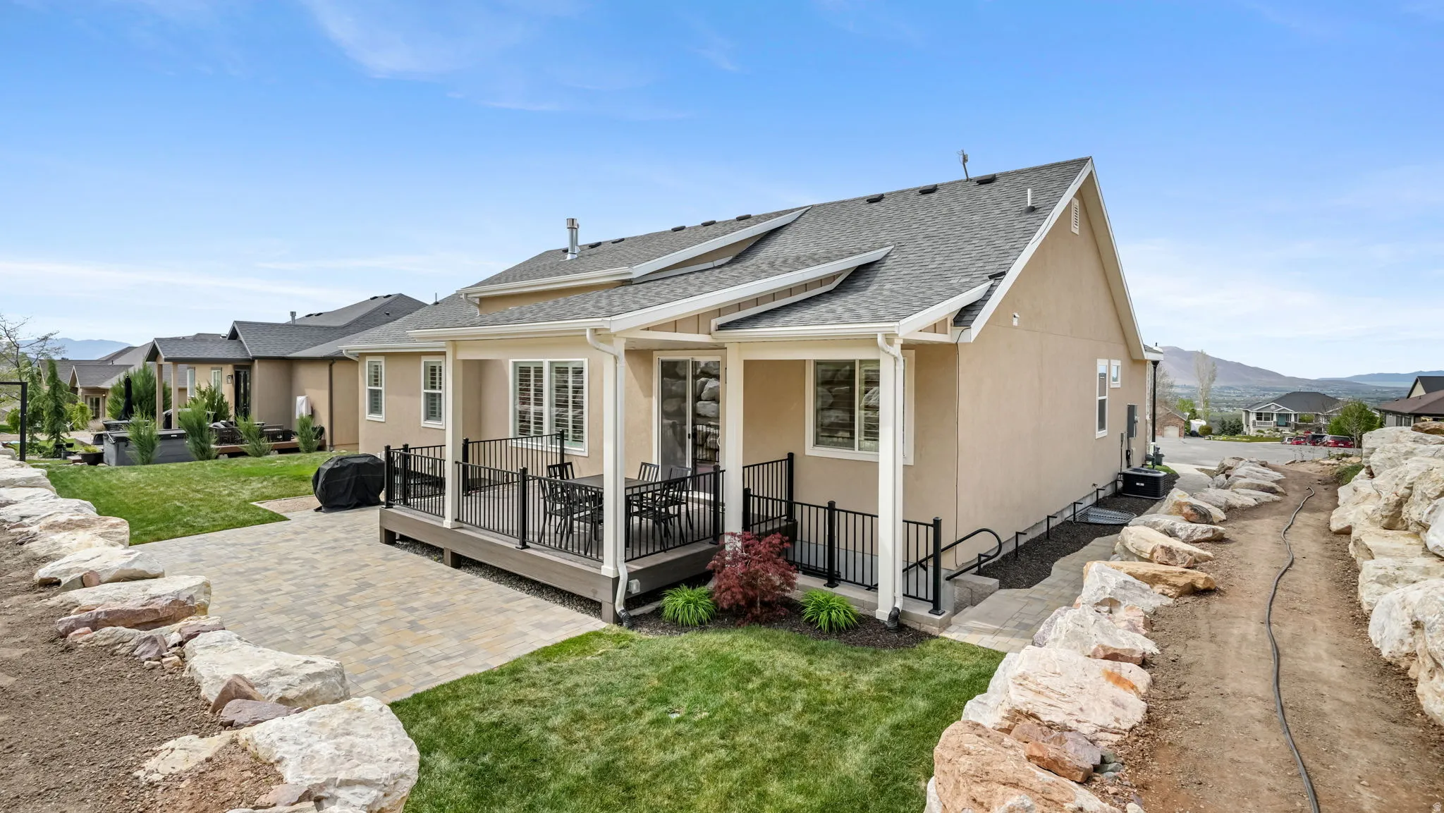 Back of house with a covered deck with mountain view, a lawn, a shingled roof, stucco siding, and a patio area