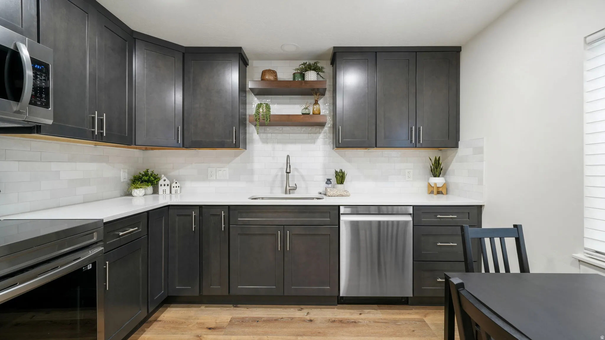 Kitchen with open shelves, stainless steel appliances, light wood-style flooring, light quartz countertops, and backsplash