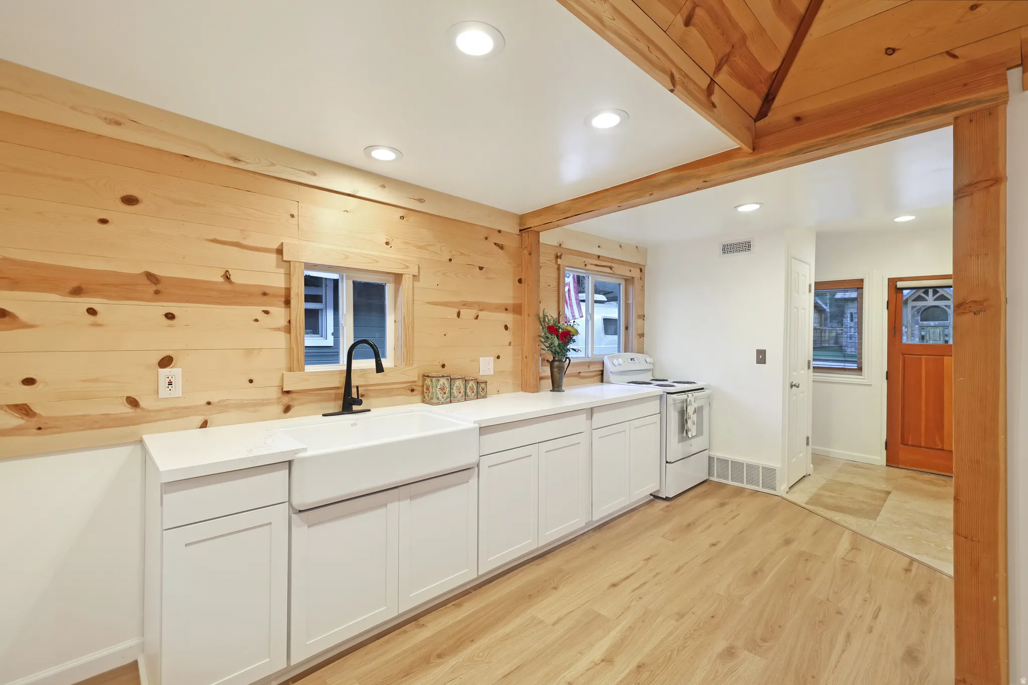 Kitchen with wood walls, light wood-type flooring, recessed lighting, white electric range oven, and white cabinets