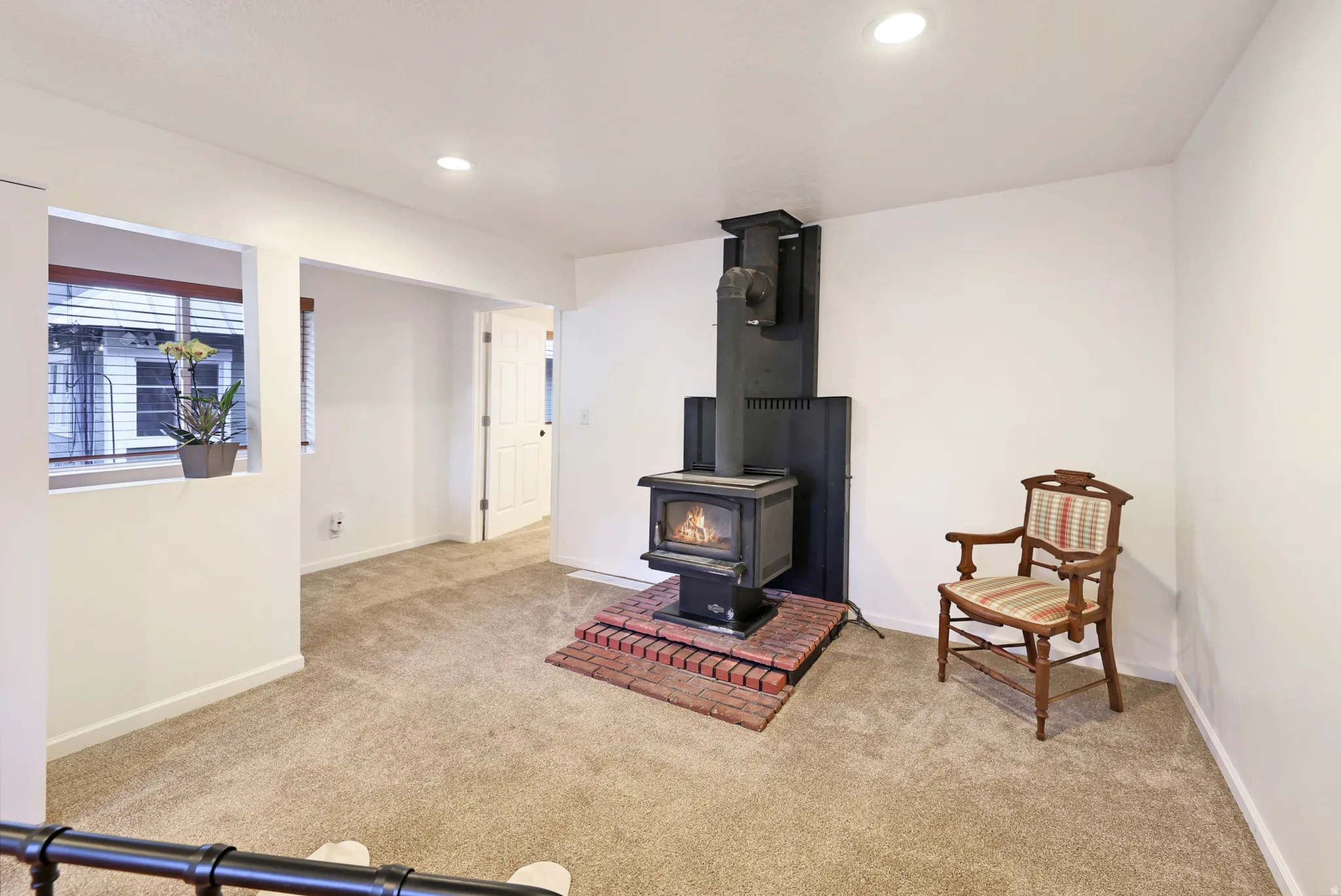 Living area featuring light colored carpet, a wood stove, and recessed lighting