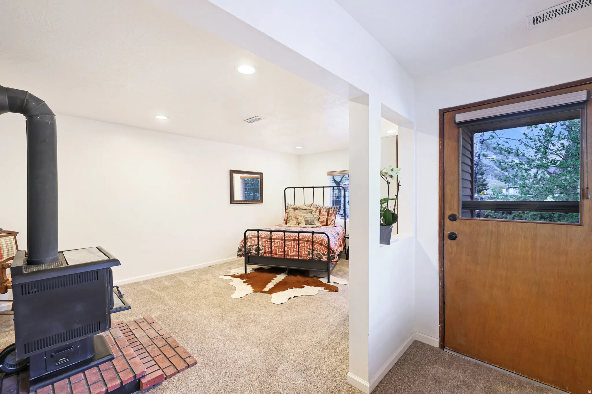 Bedroom with light colored carpet, a wood stove, multiple windows, and recessed lighting