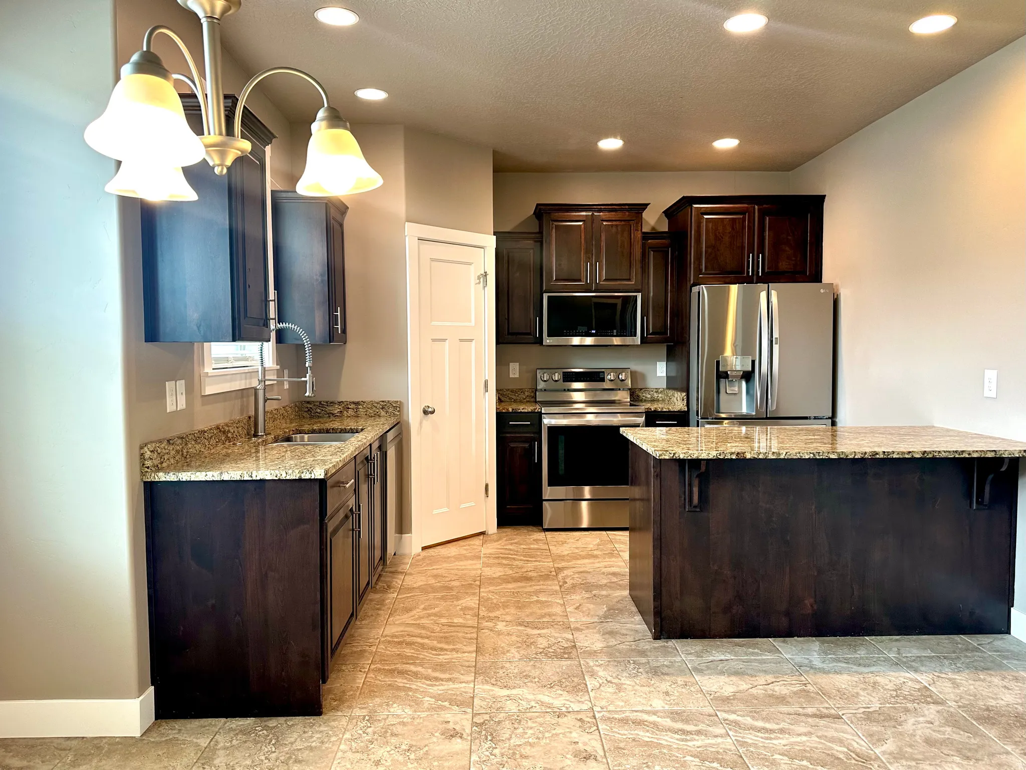 Kitchen with dark wood finish cabinets, stainless steel appliances, light stone countertops, hanging light fixtures, and a breakfast bar area