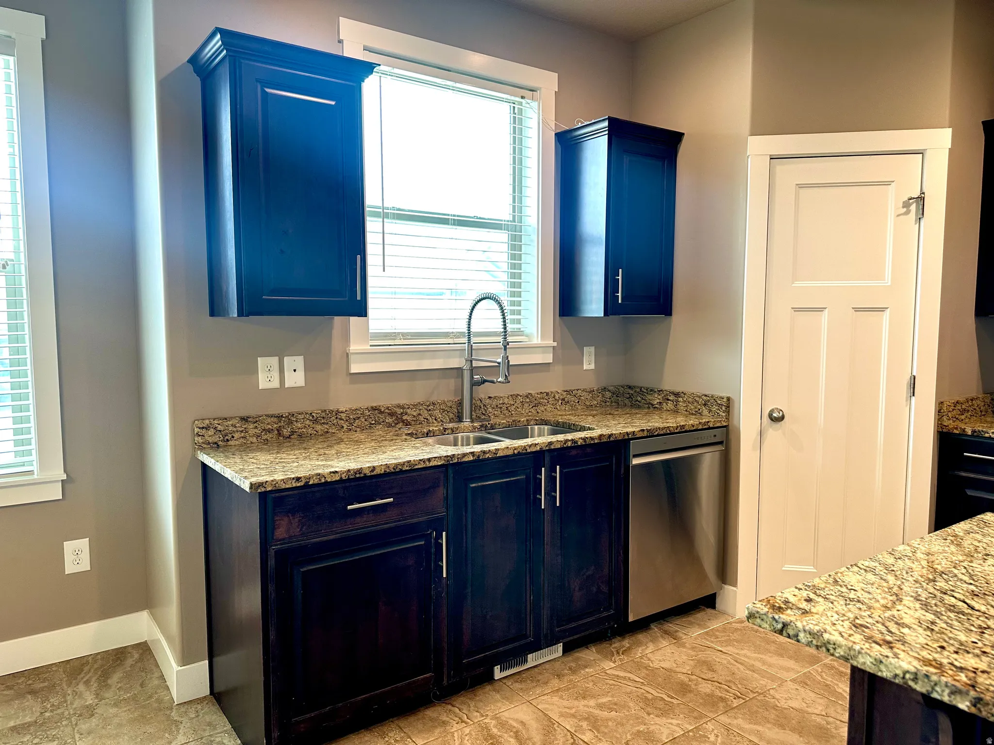 Kitchen with light stone countertops, stainless steel dishwasher, and blue cabinets