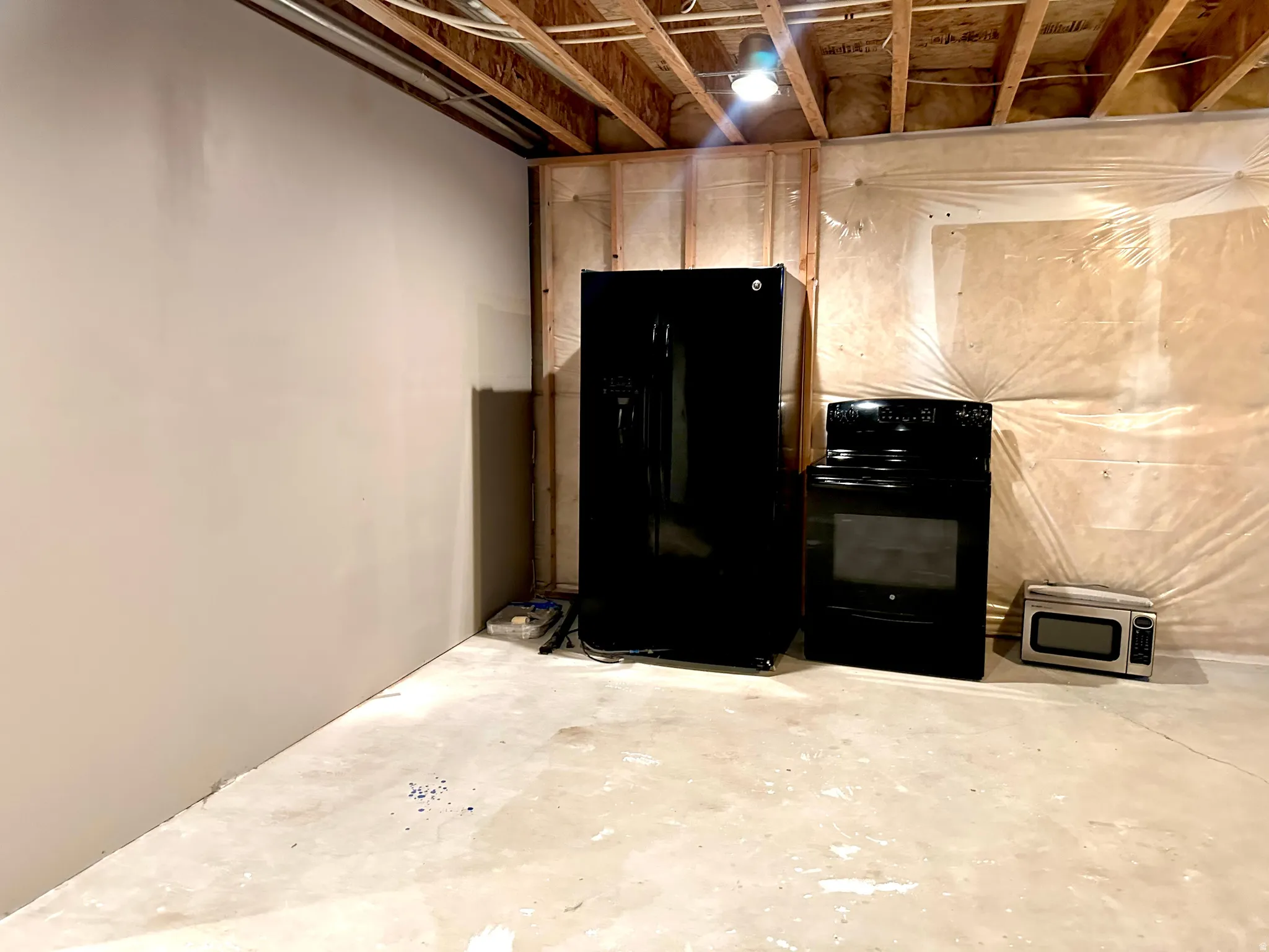 Unfinished basement with black refrigerator with ice dispenser