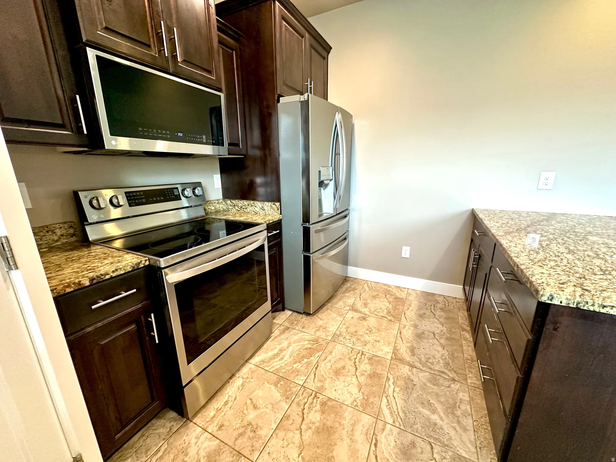 Kitchen with dark wood finish cabinets, stainless steel appliances, and light stone counters