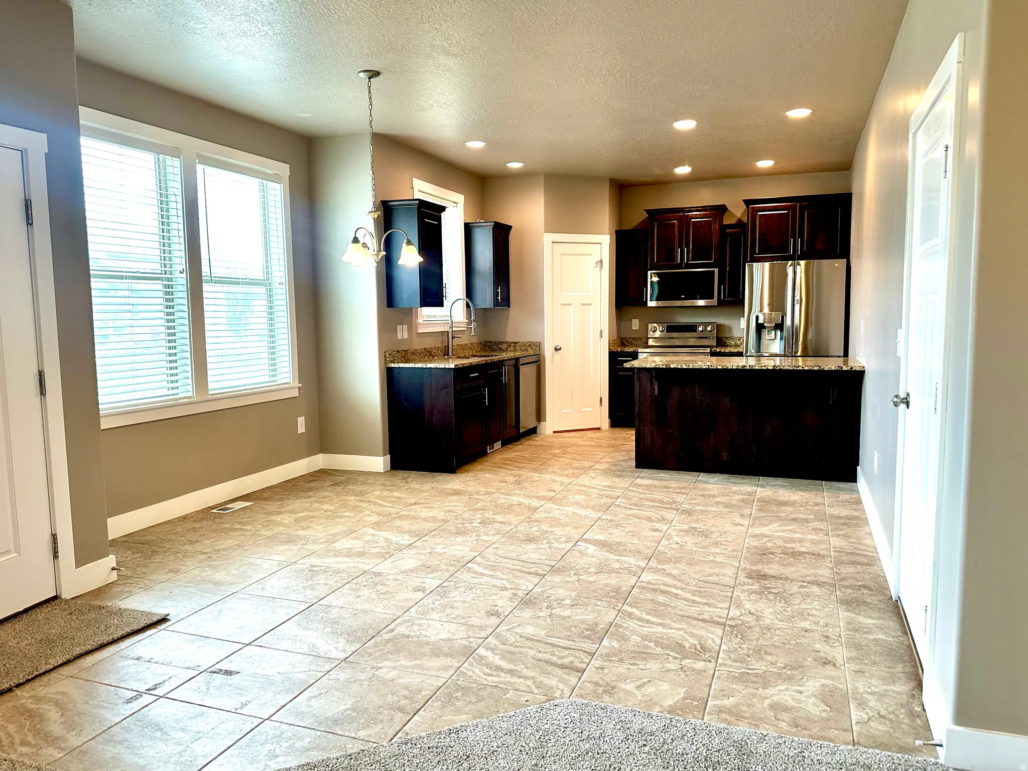 Kitchen featuring stainless steel appliances, light stone countertops, dark wood finish cabinets, a textured ceiling, and hanging light fixtures