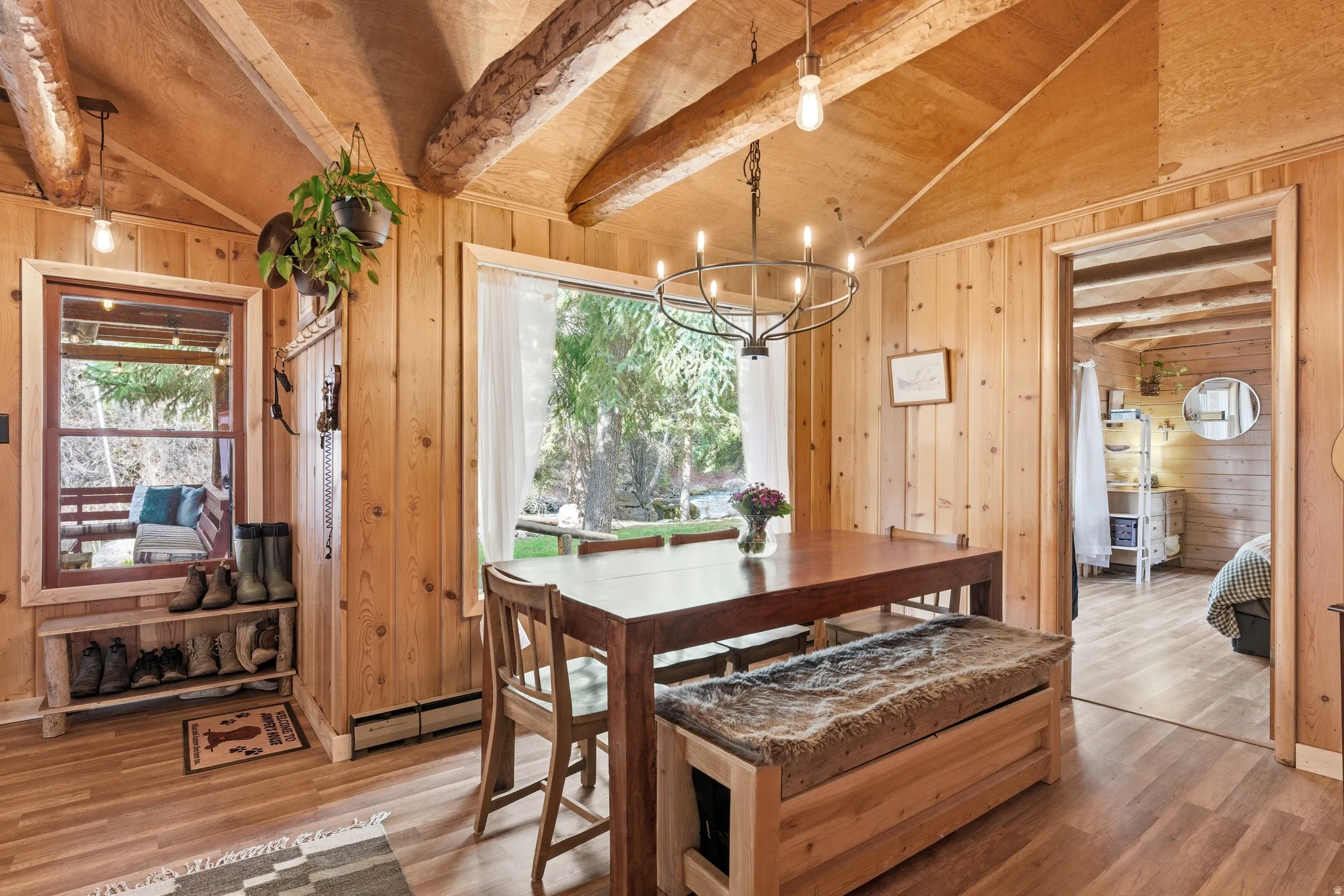 Dining area with plenty of natural light, a chandelier, vaulted ceiling with beams, light wood-style floors, and wood walls