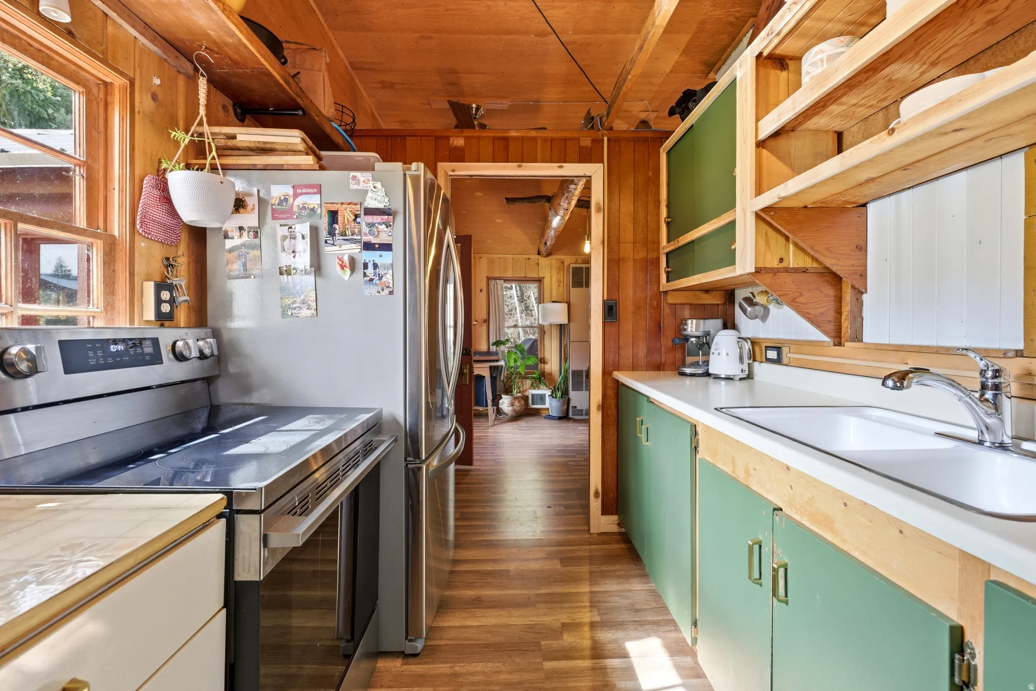 Kitchen with electric stove, wood walls, open shelves, light countertops, and dark wood-style flooring