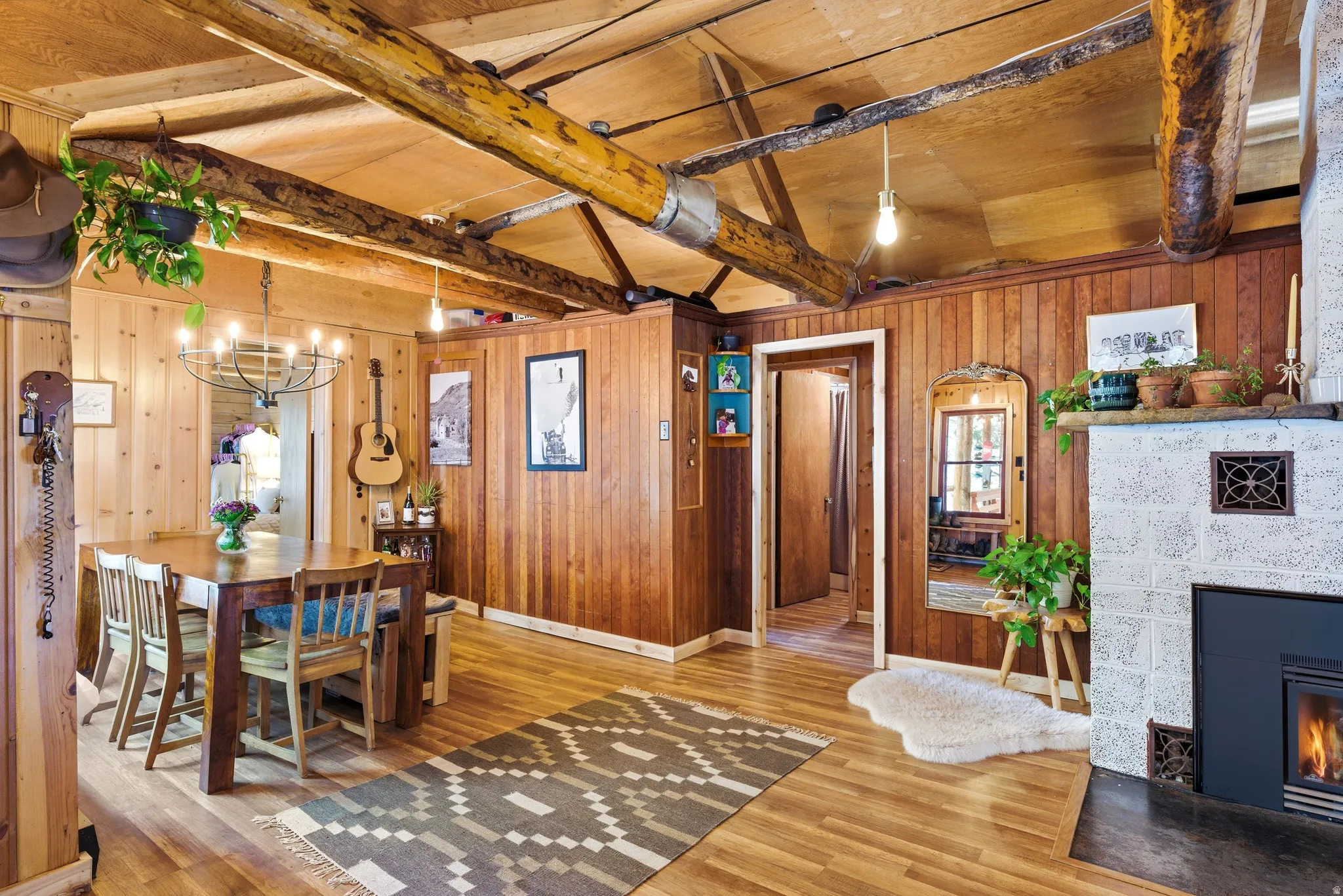 Dining space featuring vaulted ceiling with beams, wooden walls, suspended lighting, a fireplace, and wood finished floors