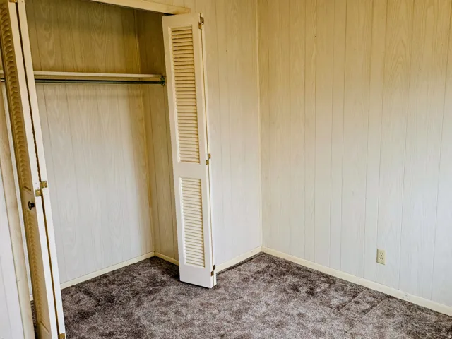 Unfurnished bedroom with wood walls, a closet, and dark colored carpet