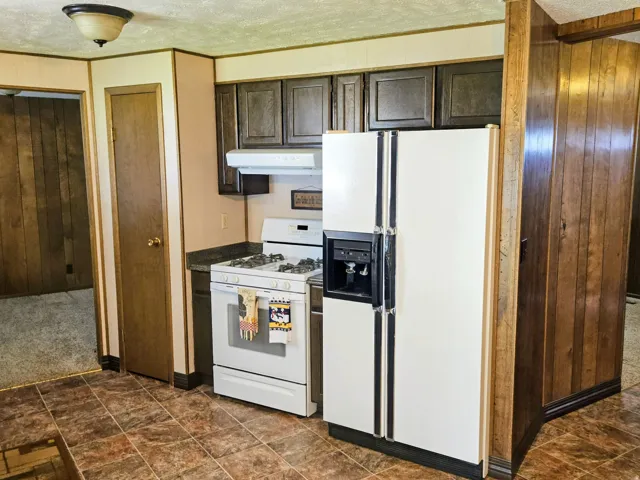 Kitchen featuring wood walls, white appliances, dark wood finish cabinetry, a textured ceiling, and dark countertops