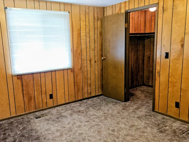 Unfurnished bedroom with a spacious closet, wooden walls, and carpet