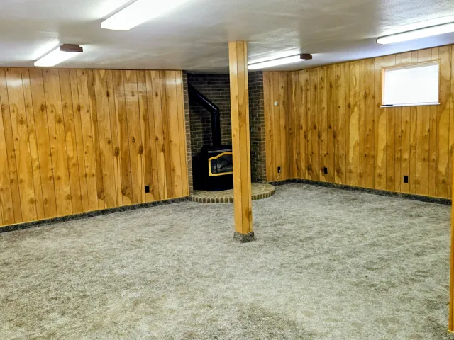 Below grade area featuring carpet flooring, wooden walls, and a wood stove