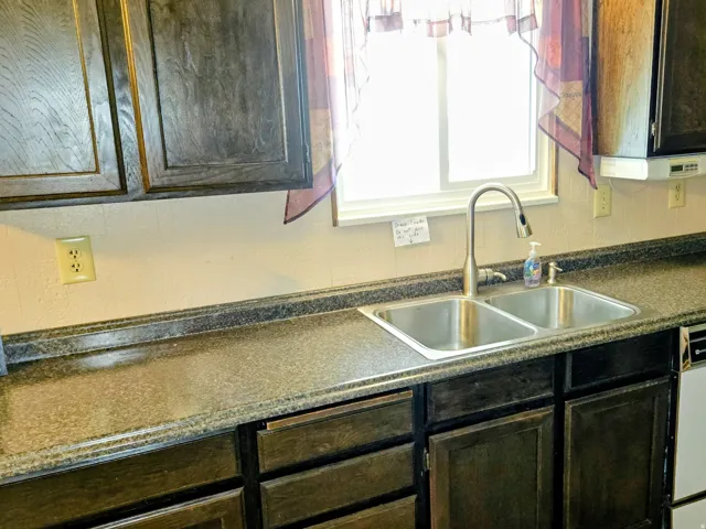 Kitchen featuring dark countertops, white dishwasher, and dark wood finish cabinetry
