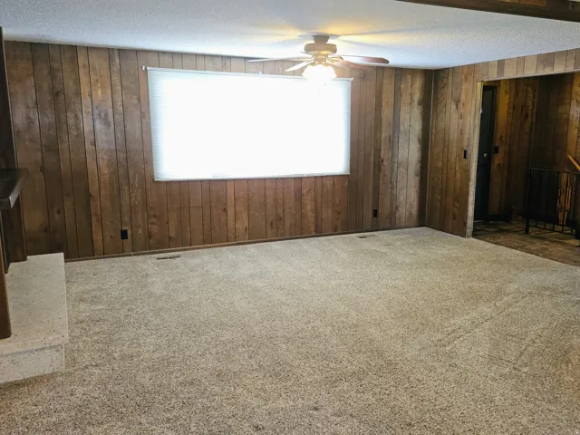 Unfurnished living room featuring carpet, ceiling fan, wooden walls, and a textured ceiling