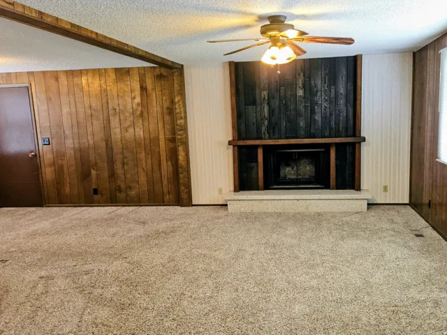 Unfurnished living room featuring carpet, wood walls, a ceiling fan, a fireplace, and a textured ceiling