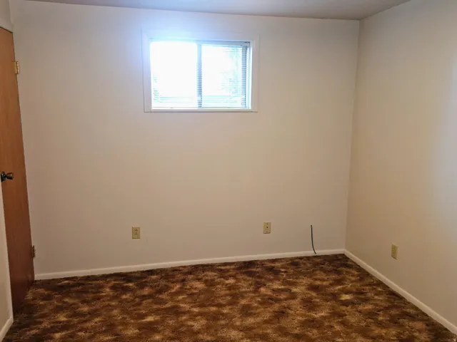 Empty room featuring dark colored carpet and baseboards