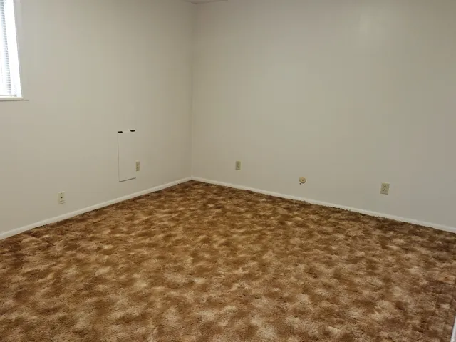 Spare room featuring dark carpet and baseboards