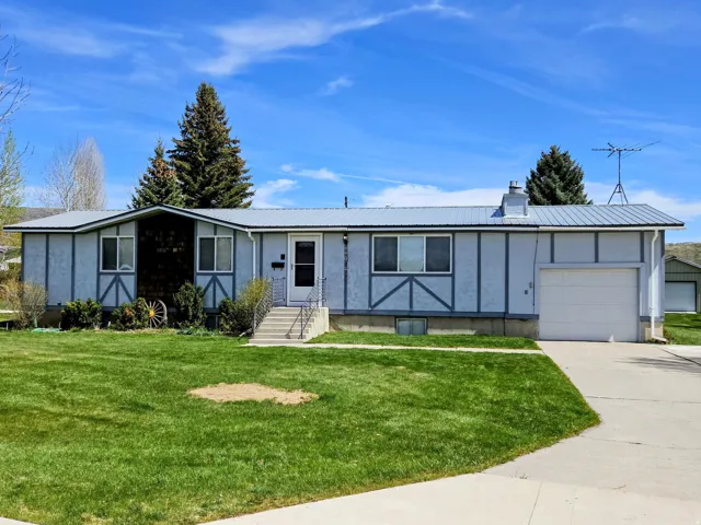 Ranch-style home with a metal roof, board and batten siding, a front yard, an attached garage, and driveway