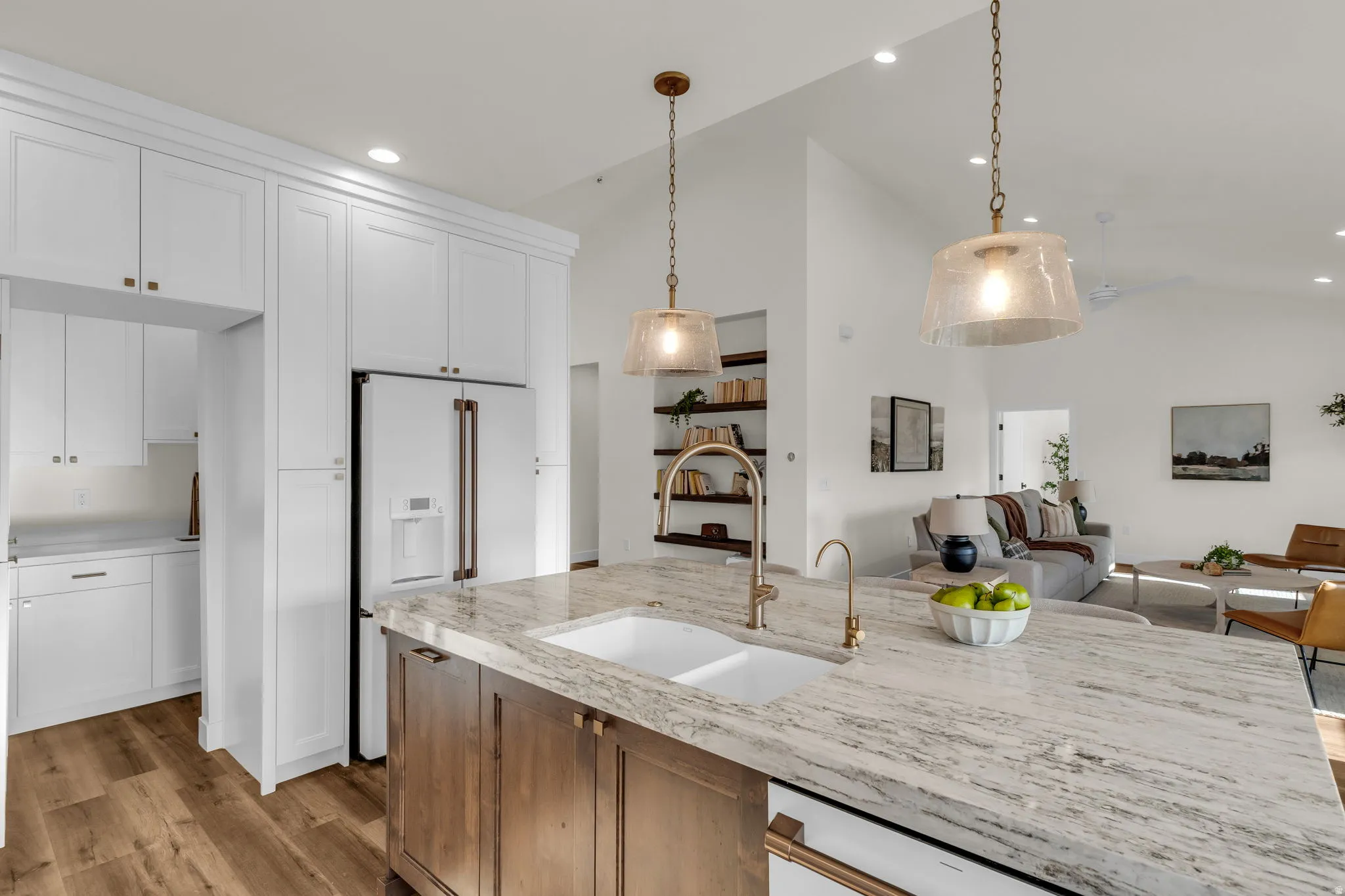 Kitchen featuring two tone cabinetry, light stone counters, white appliances, light wood finished floors, and open floor plan