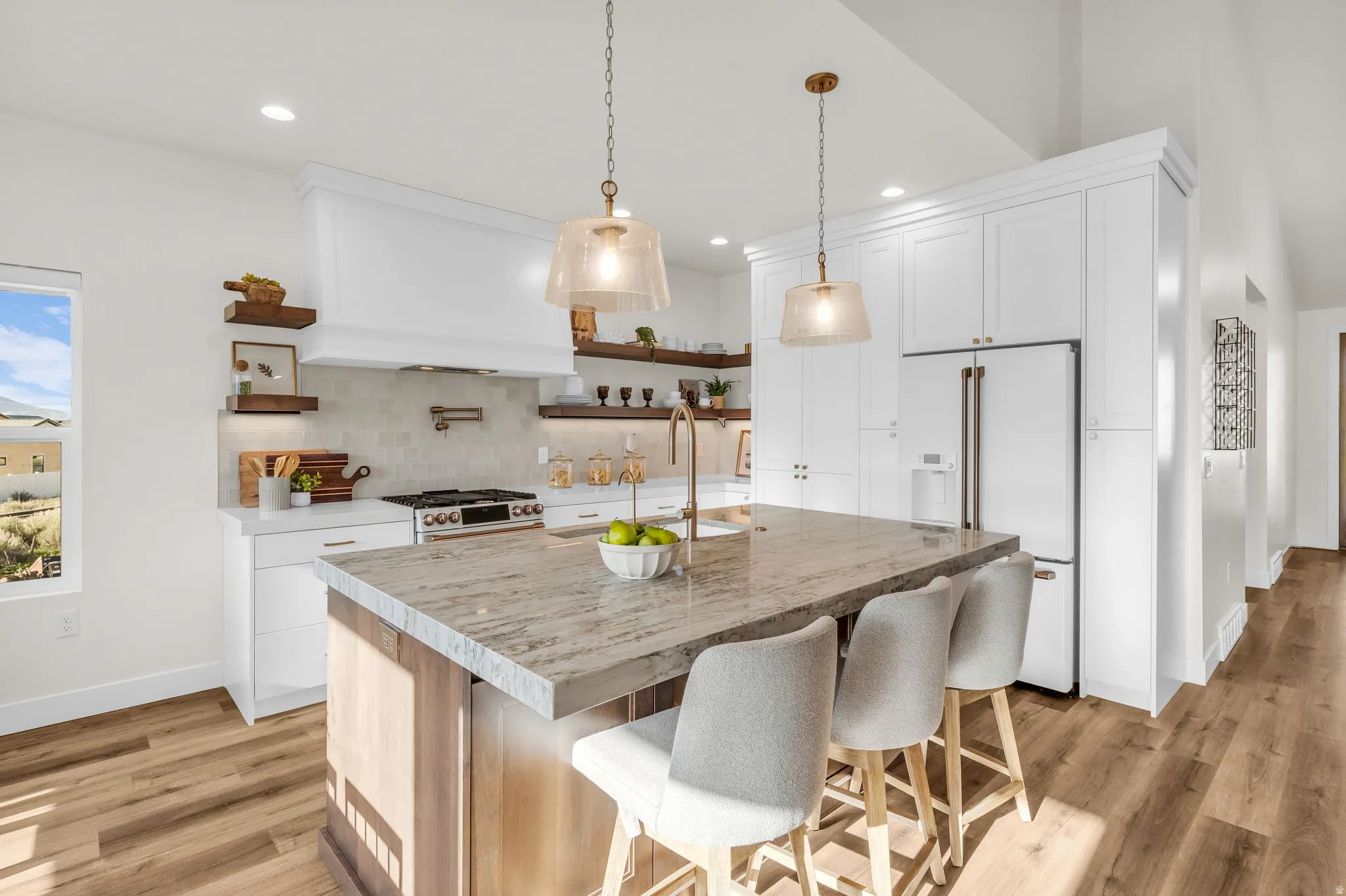 Kitchen featuring open shelves, premium appliances, a kitchen bar, light wood-style flooring, and a kitchen island with sink