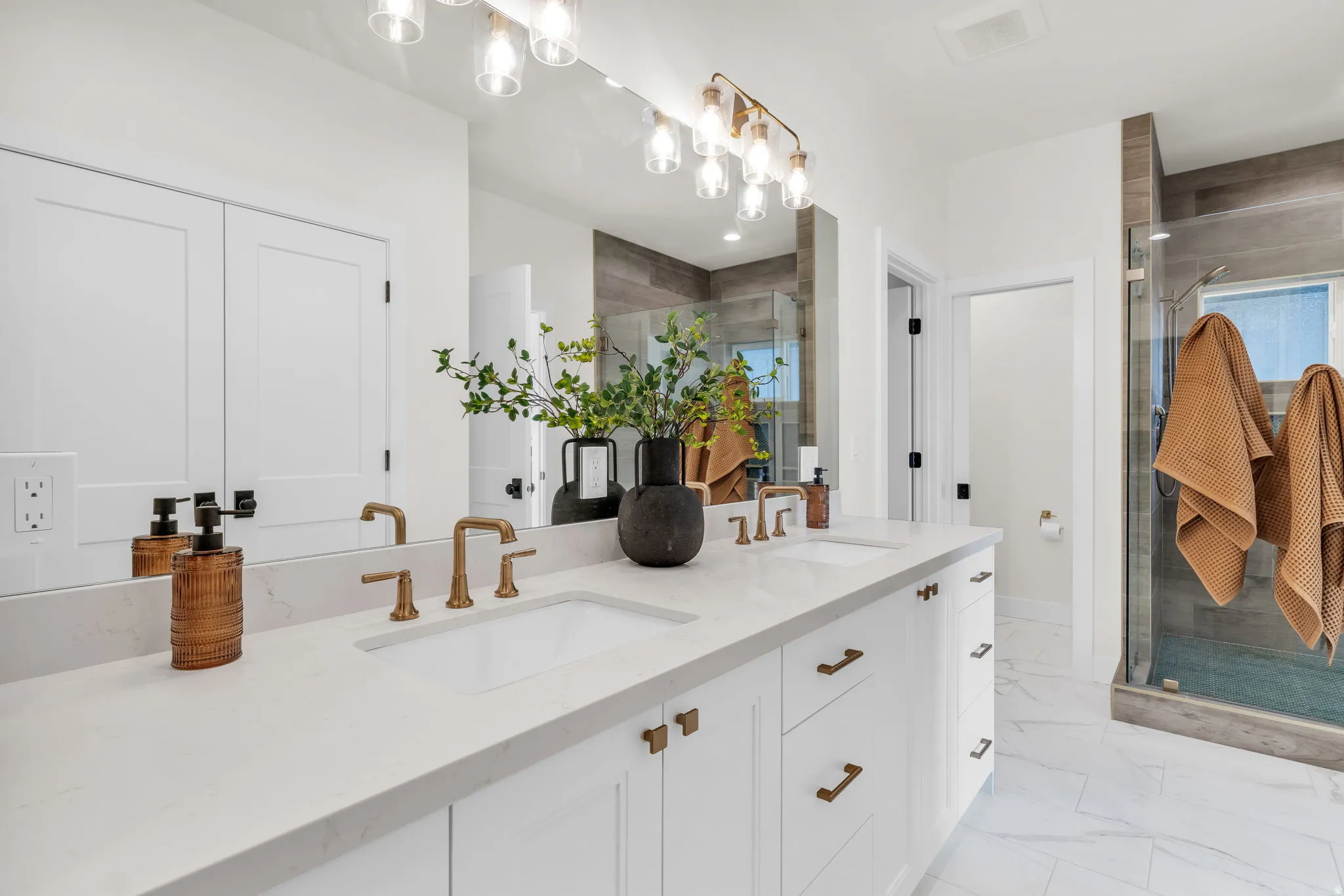Full bathroom featuring double vanity, a stall shower, and light marble finish flooring
