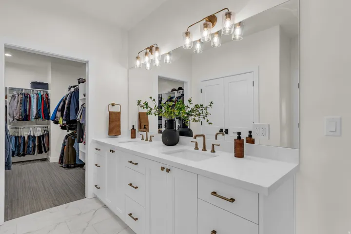 Full bath featuring double vanity, a spacious closet, and light marble finish floors
