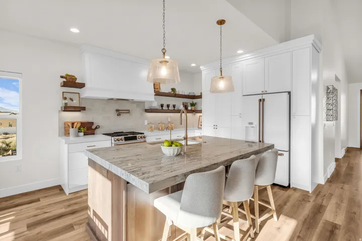 Kitchen featuring open shelves, premium appliances, a kitchen bar, light wood-style flooring, and a kitchen island with sink
