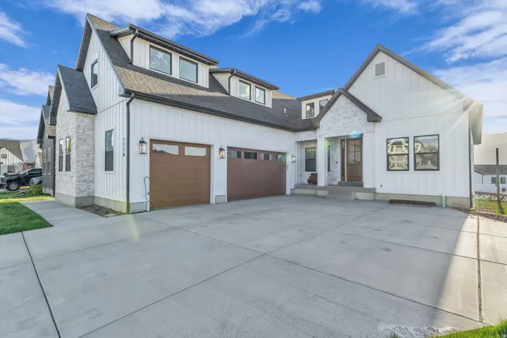 Modern farmhouse style home with stone siding, a shingled roof, concrete driveway, and board and batten siding