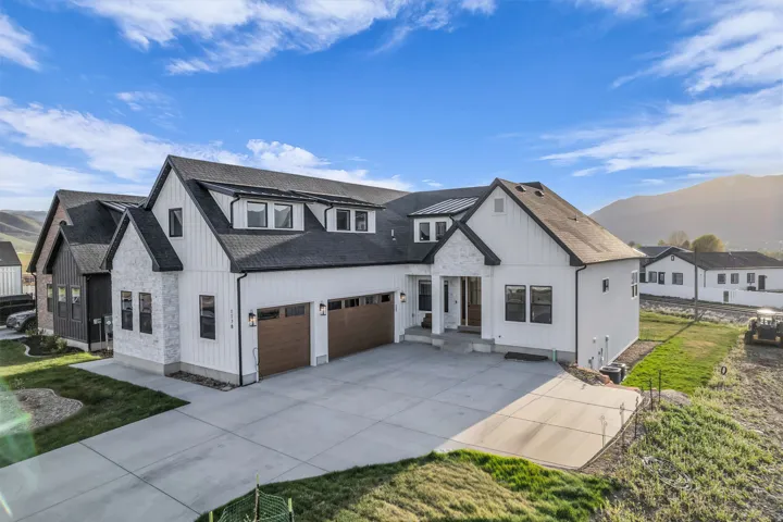 Modern farmhouse featuring concrete driveway, board and batten siding, roof with shingles, a front yard, and stone siding