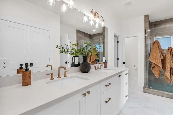 Full bathroom featuring double vanity, a stall shower, and light marble finish flooring