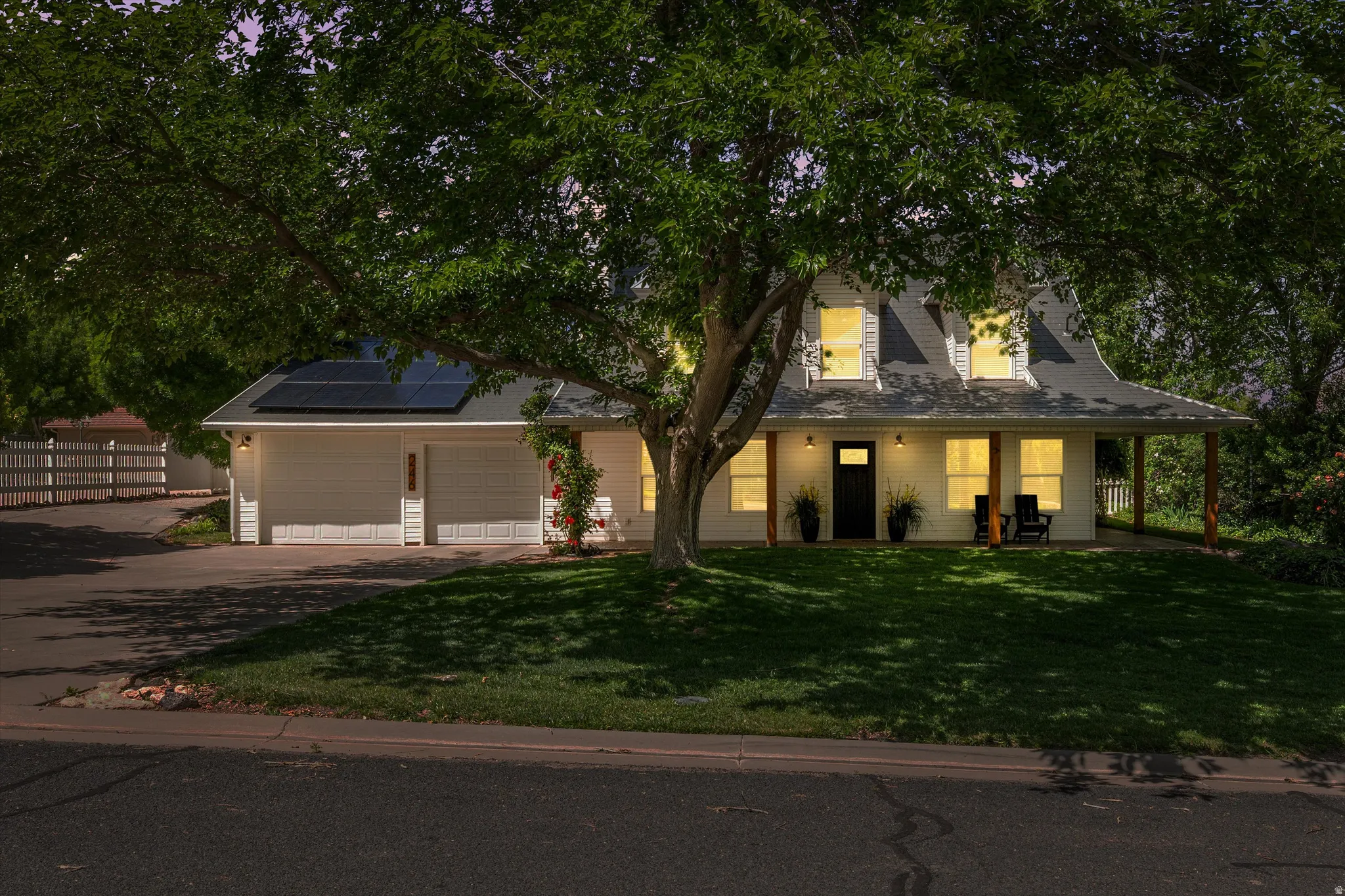 View of front of home with solar panels, covered porch, driveway, a front yard, and an attached garage