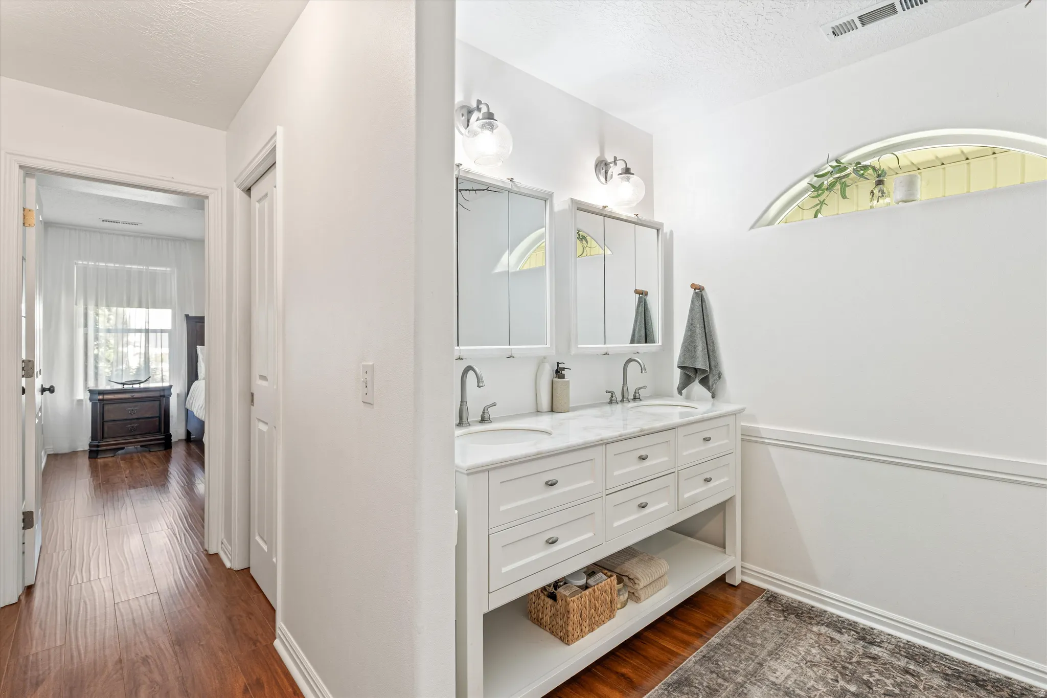 Ensuite bathroom featuring dark wood-style flooring, double vanity, and a textured ceiling