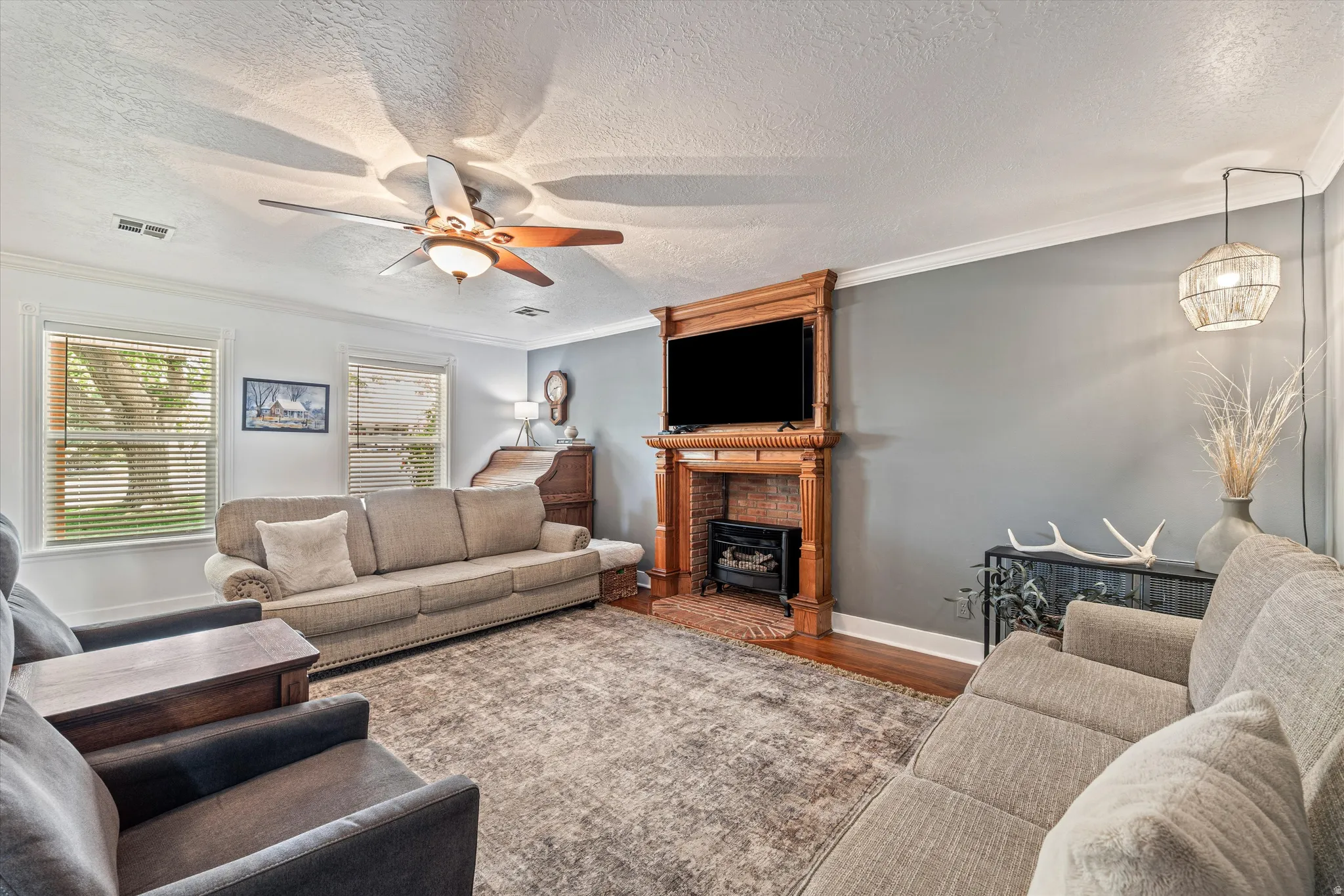 Living room featuring ornamental molding, a textured ceiling, wood finished floors, and ceiling fan
