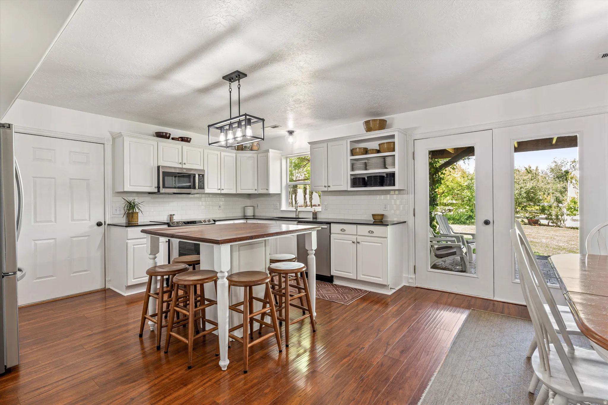 Kitchen with a breakfast bar, stainless steel appliances, decorative light fixtures, dark wood-type flooring, and white cabinetry