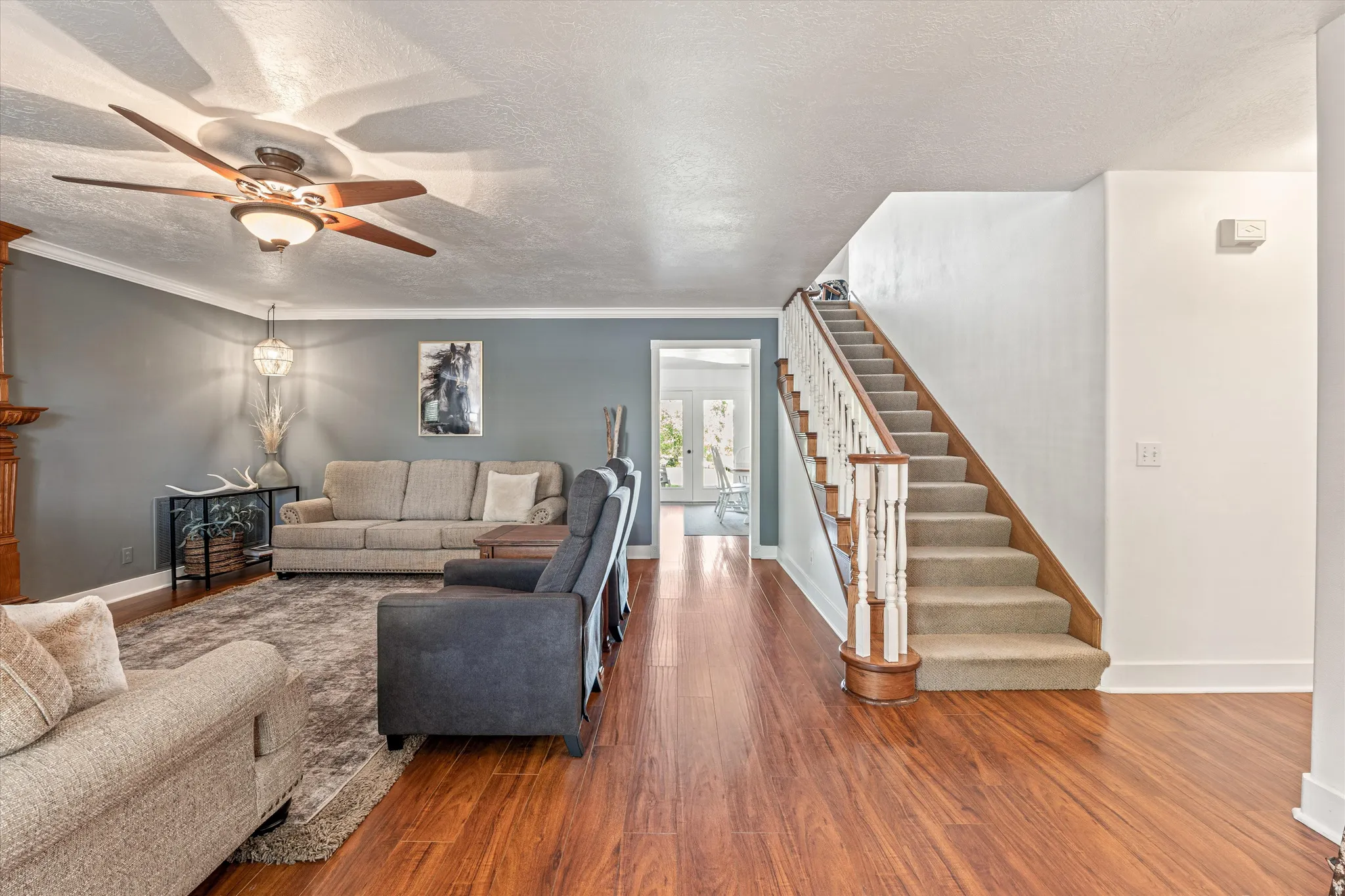 Living area featuring a textured ceiling, wood finished floors, a ceiling fan, and crown molding